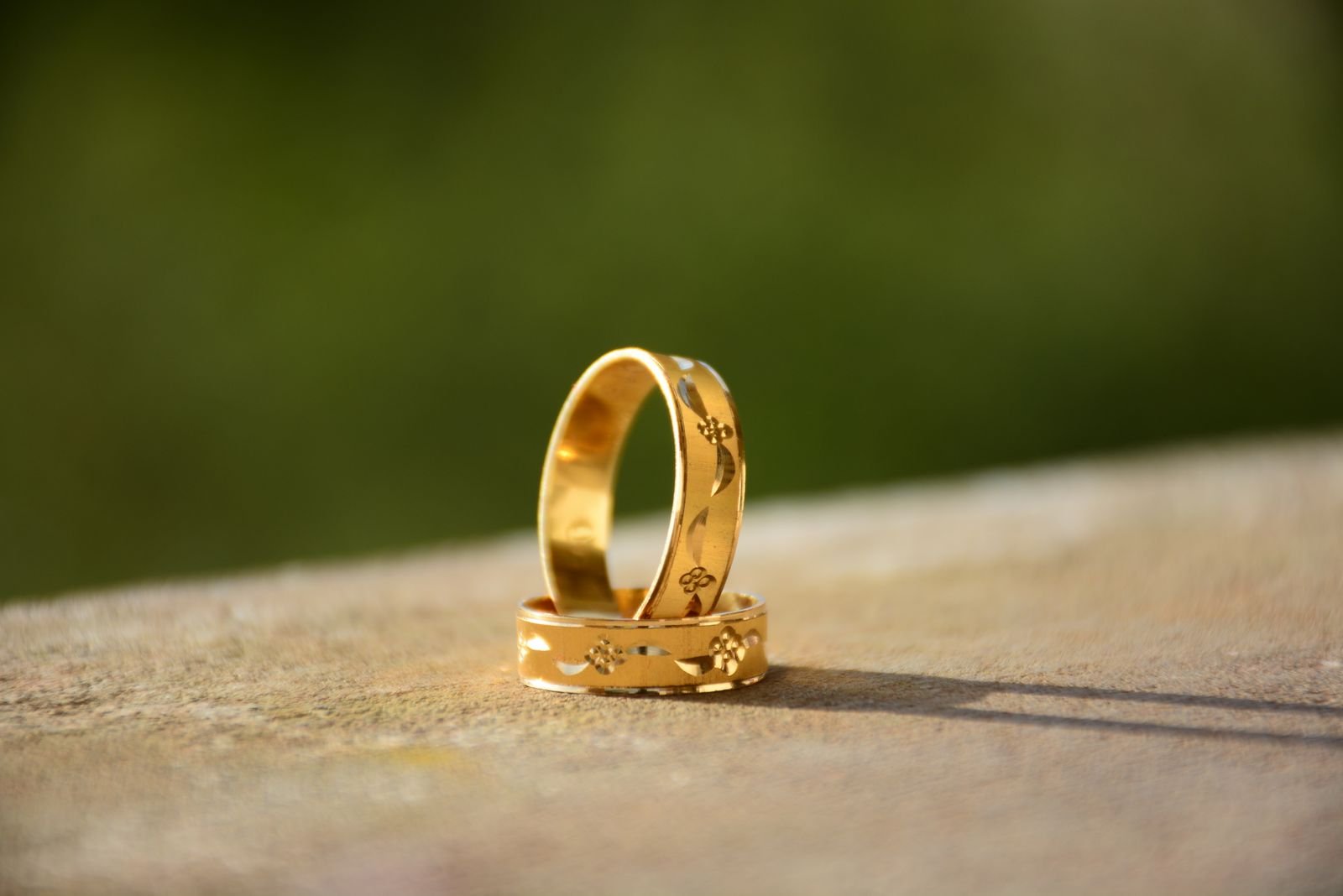 Two gold wedding bands resting on sunlit stone