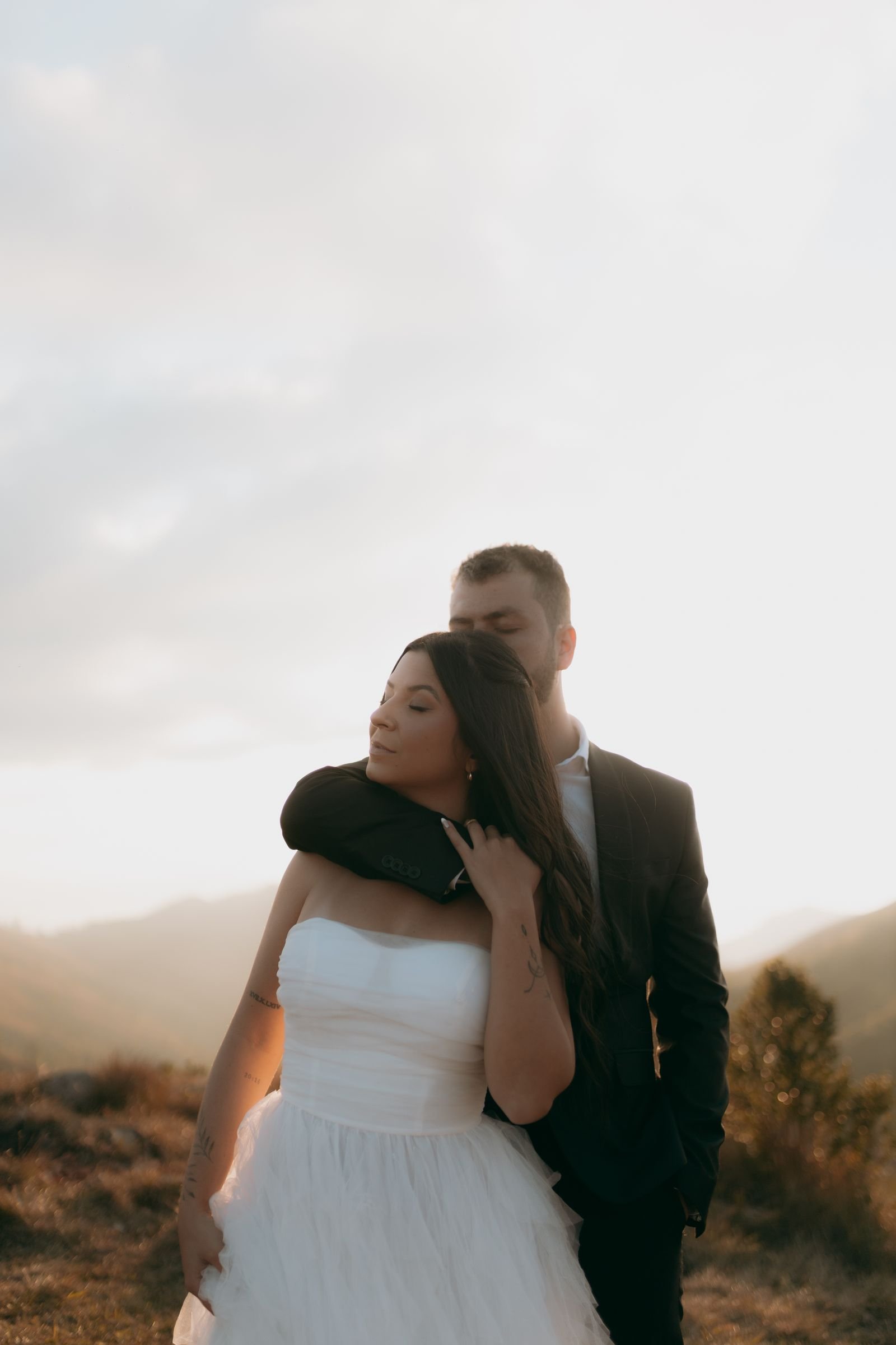 The couple embracing on a mountainside at golden sunset