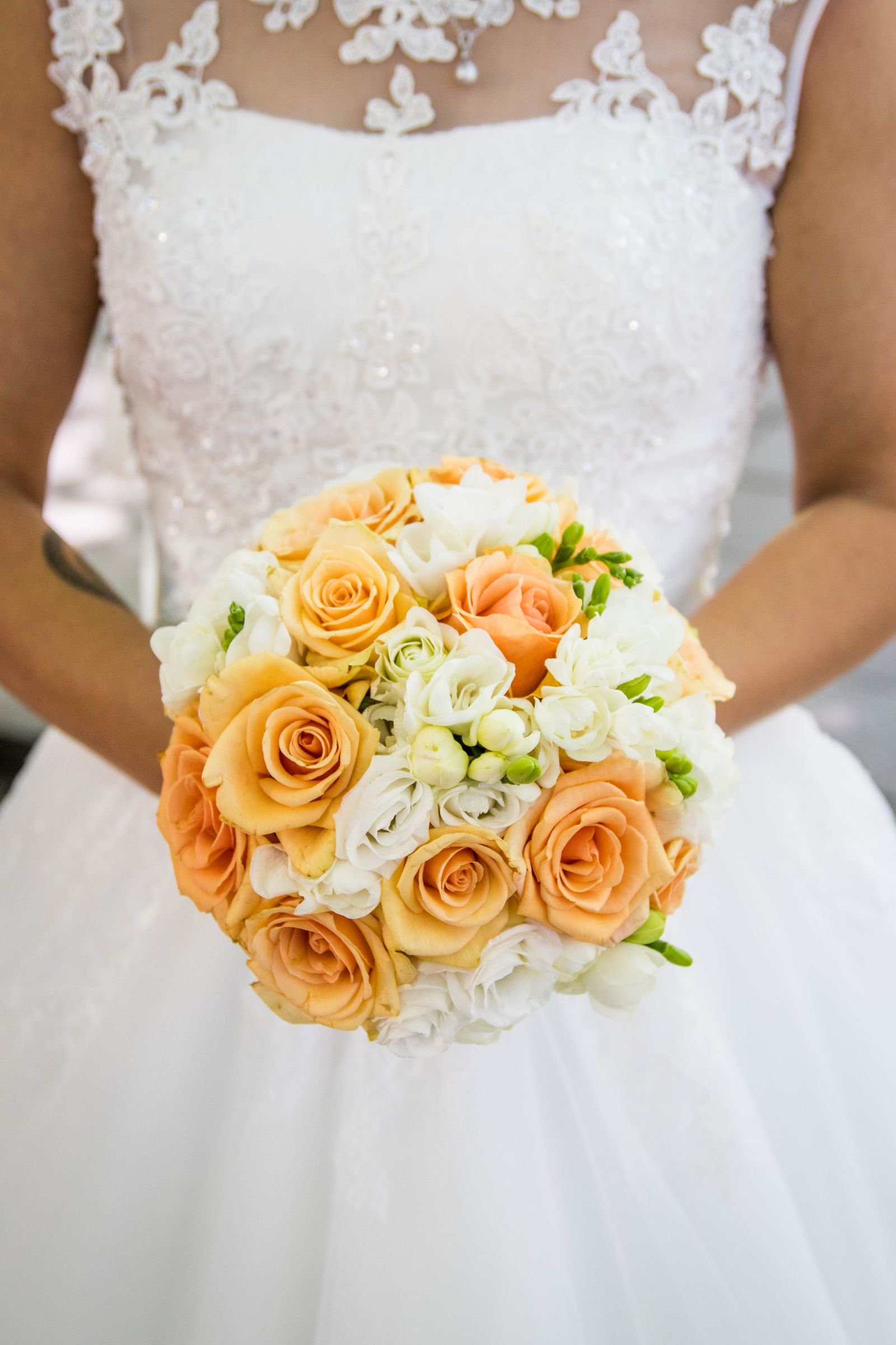 The bridal bouquet of peach and white roses held against the lace gown