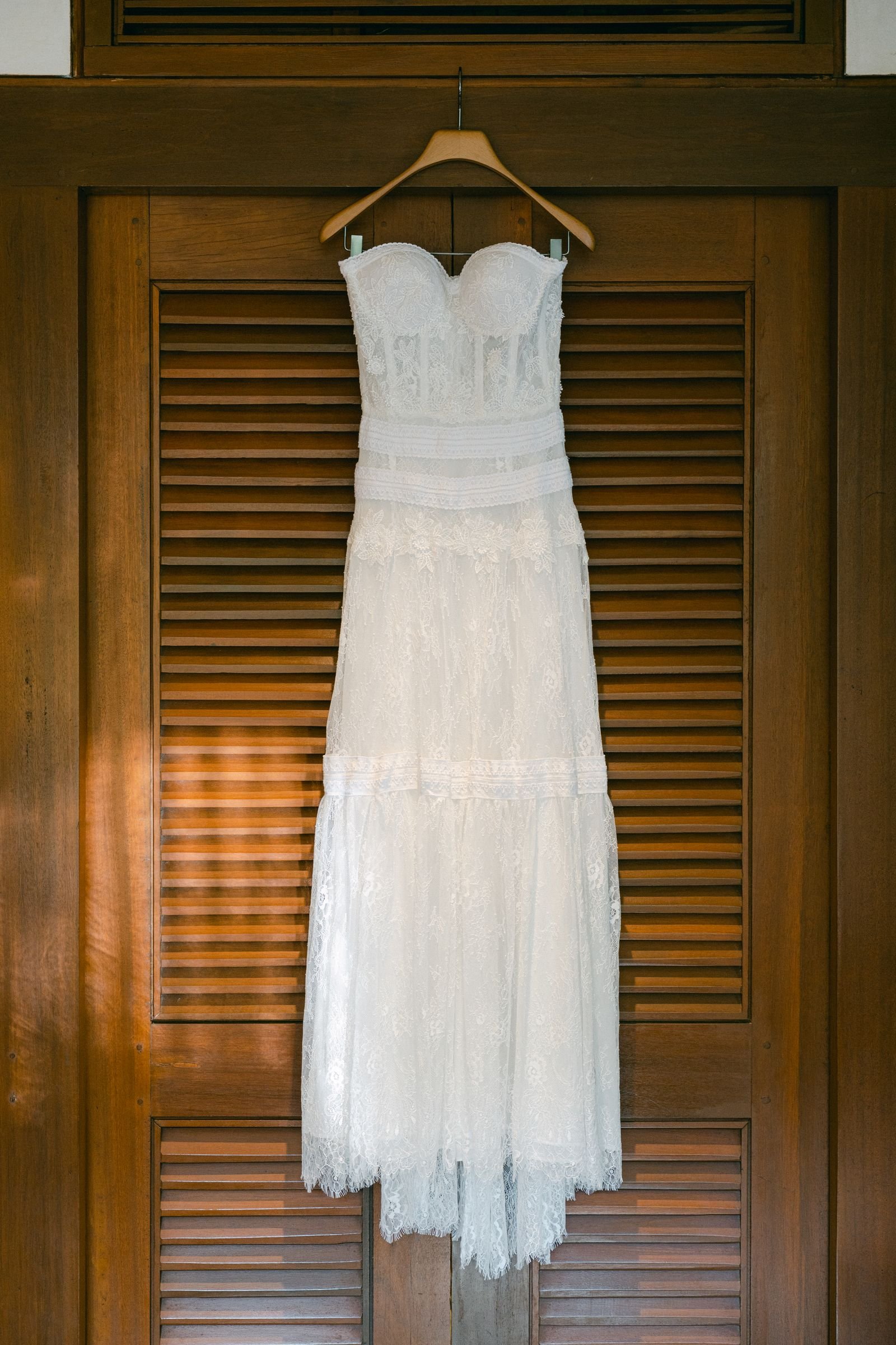 The lace wedding dress hanging against warm wooden shutters