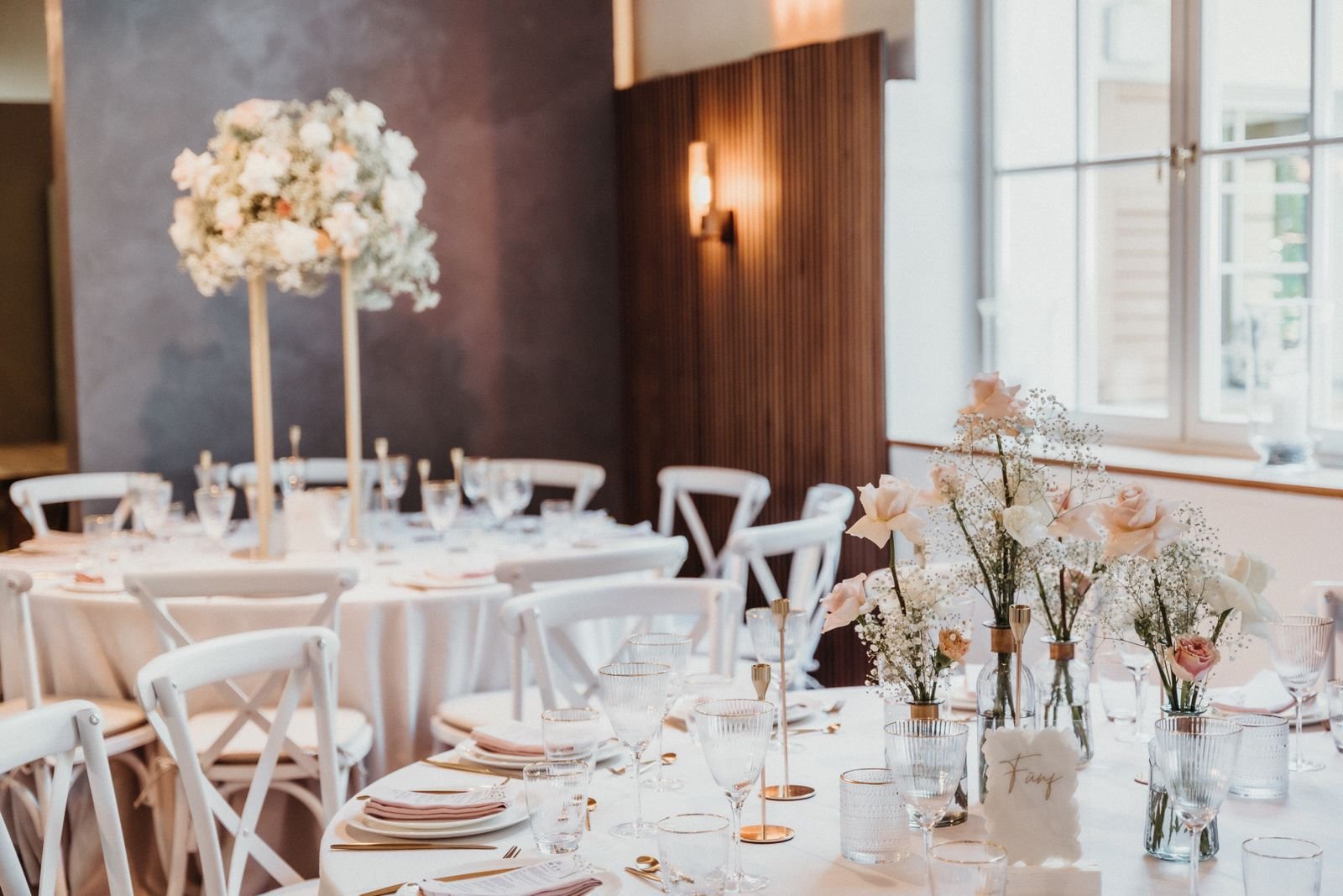Reception tables dressed in white linen, blush napkins, and roses